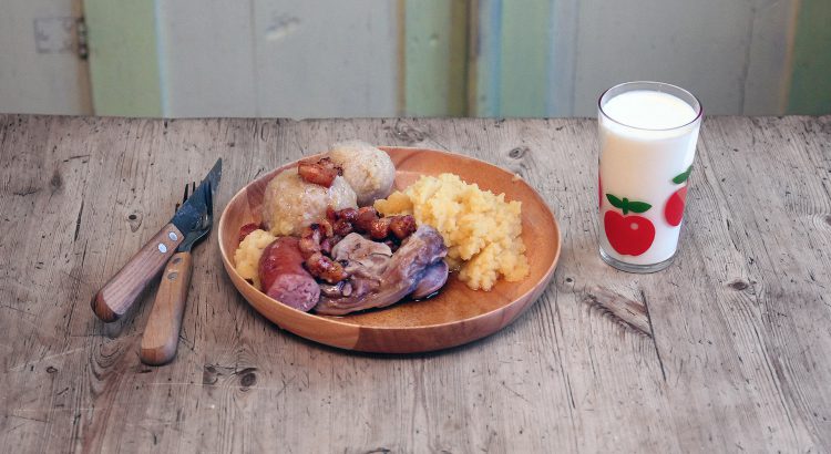 Picture of a plate of raspeball, sausage, sweed mash toppet with bacon served on an old wooden table in an old norwegian wooden hut.